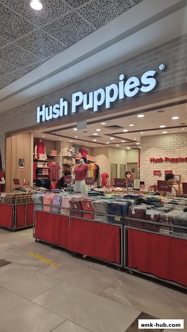 The Hush Puppies store entrance displays colorful t-shirts and apparel on racks and mannequins.