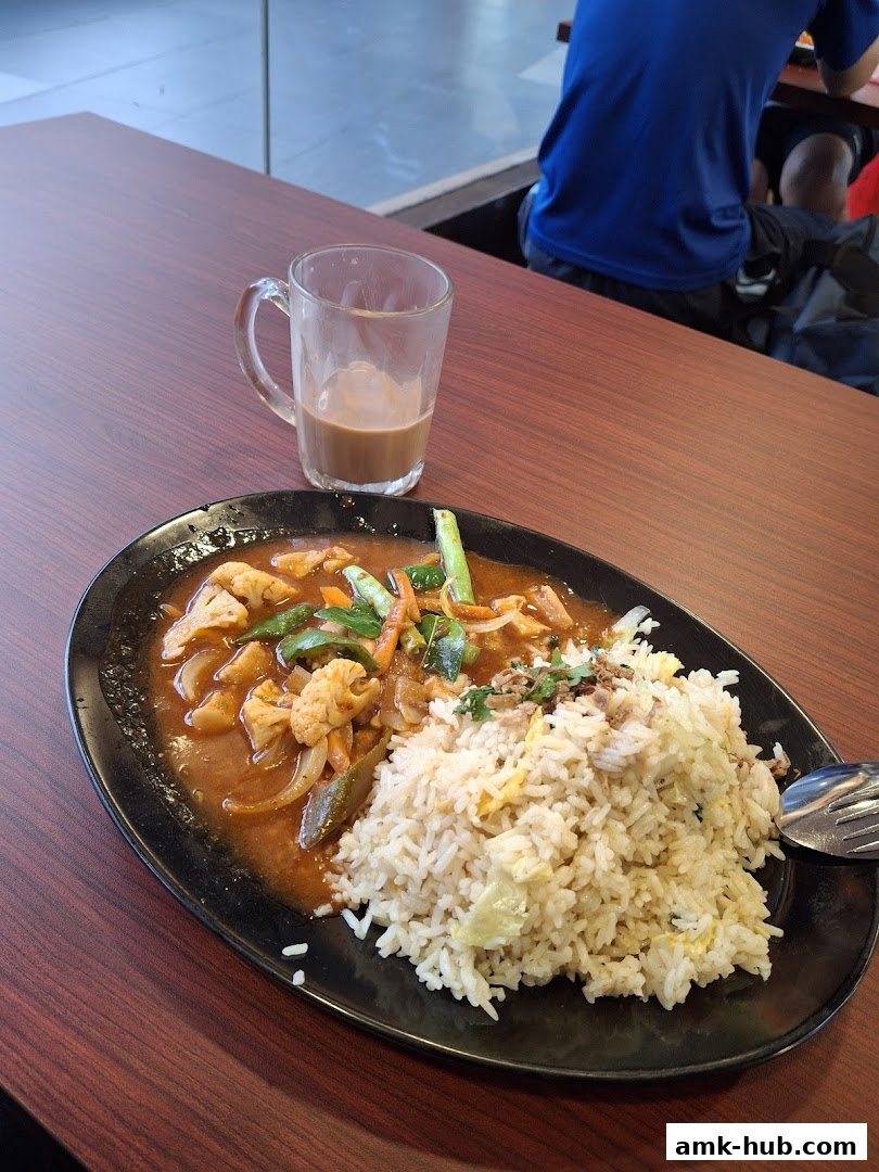 A plate of fried rice with curry and a glass of milk tea on a wooden table.