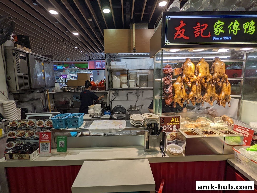 A food stall displaying roasted ducks and various dishes, with staff preparing food in the background.