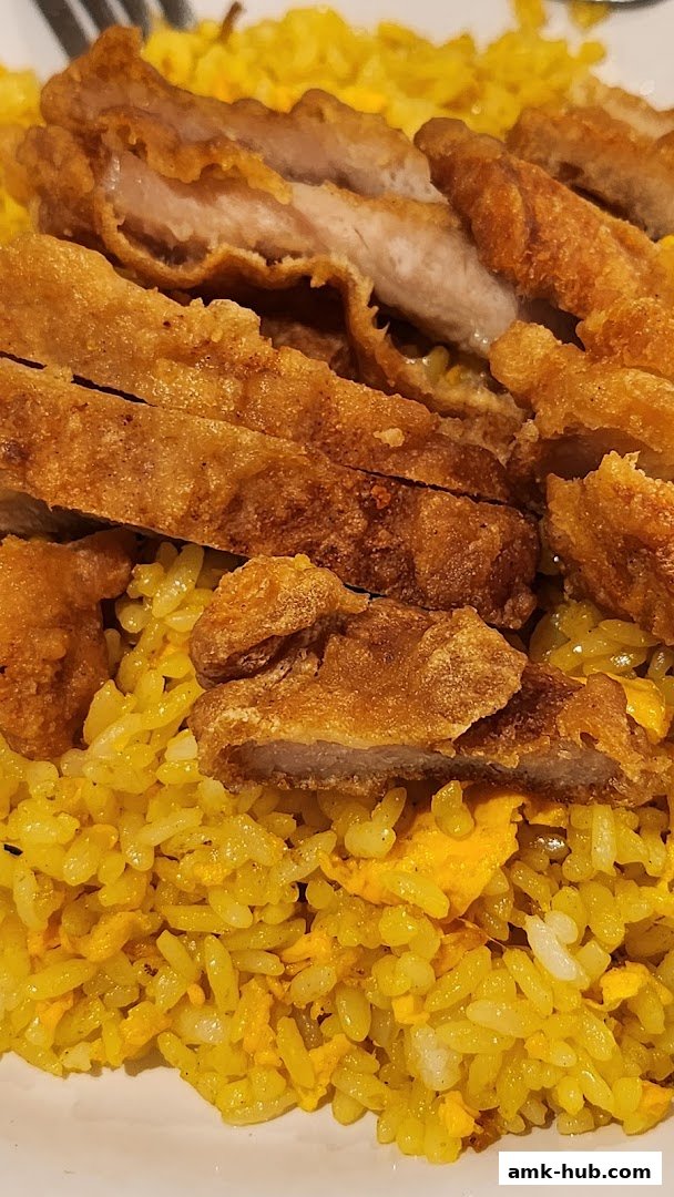 A close-up shot of crispy fried pork slices served over fragrant yellow rice.