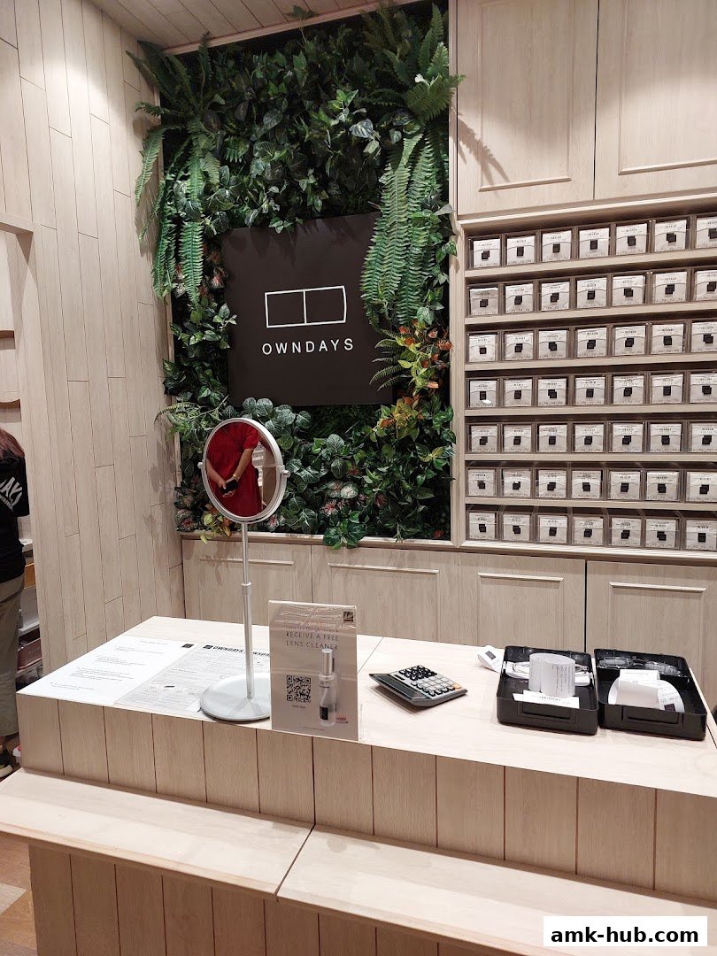 Interior shot of OWNDAYS AMK Hub with a green wall, logo, and display shelves.