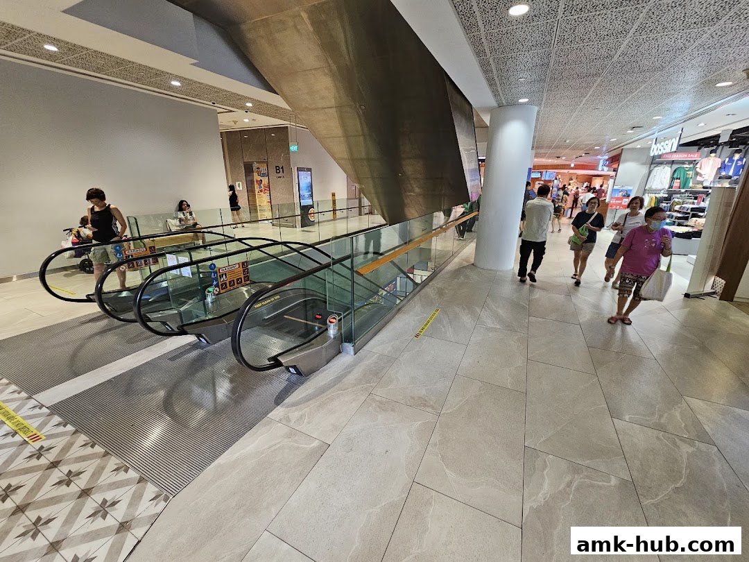 People walking on escalators and in a shopping mall corridor with shops visible.
