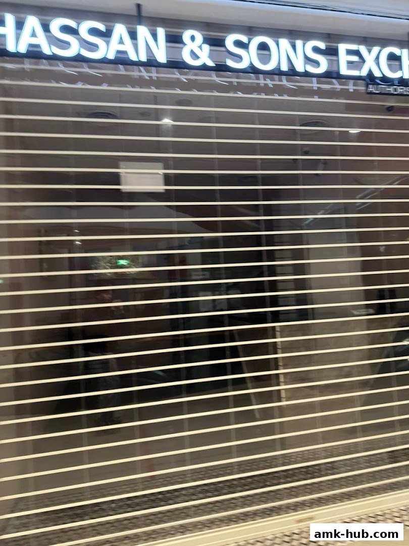 The exterior of Hassan & Sons Exchange with its sign illuminated and the security shutter down.