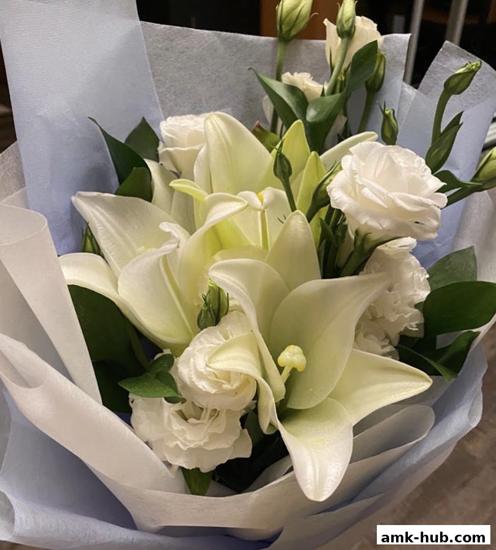 A beautiful bouquet of white lilies and roses, elegantly wrapped in light blue and white paper.