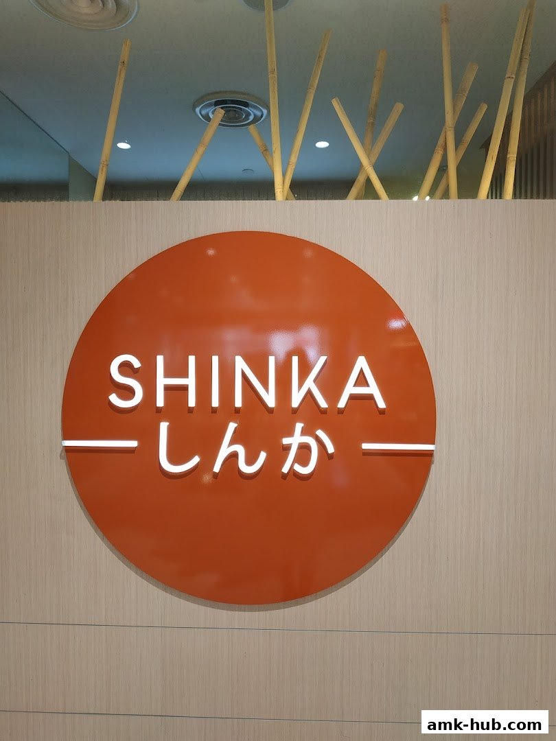 The Shinka shop logo is displayed on an orange circular sign against a wood-paneled wall.