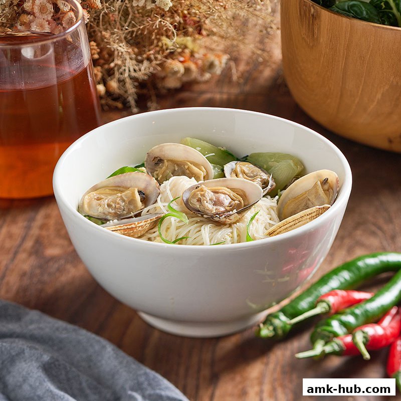 A bowl of clam noodle soup with vegetables and a glass of iced tea.