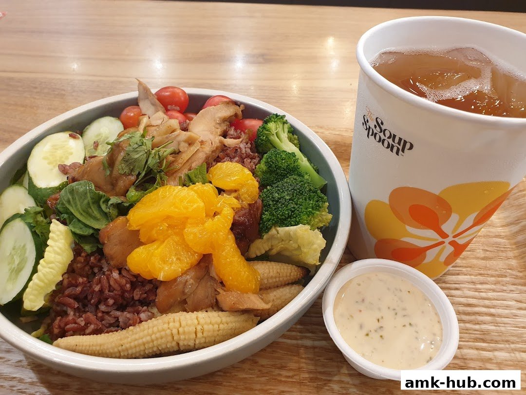 A healthy salad bowl with chicken, oranges, and vegetables, served with a drink and dip.