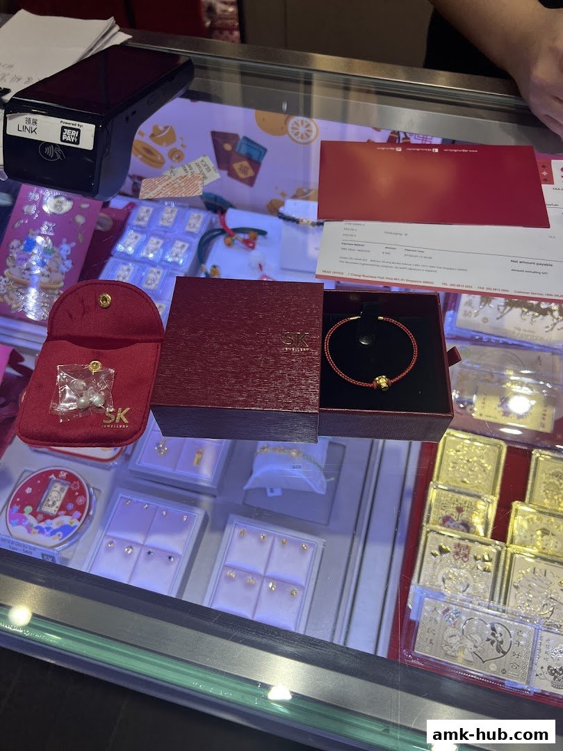 A display case filled with SK Jewellery, including gold bars, earrings, and a bracelet.