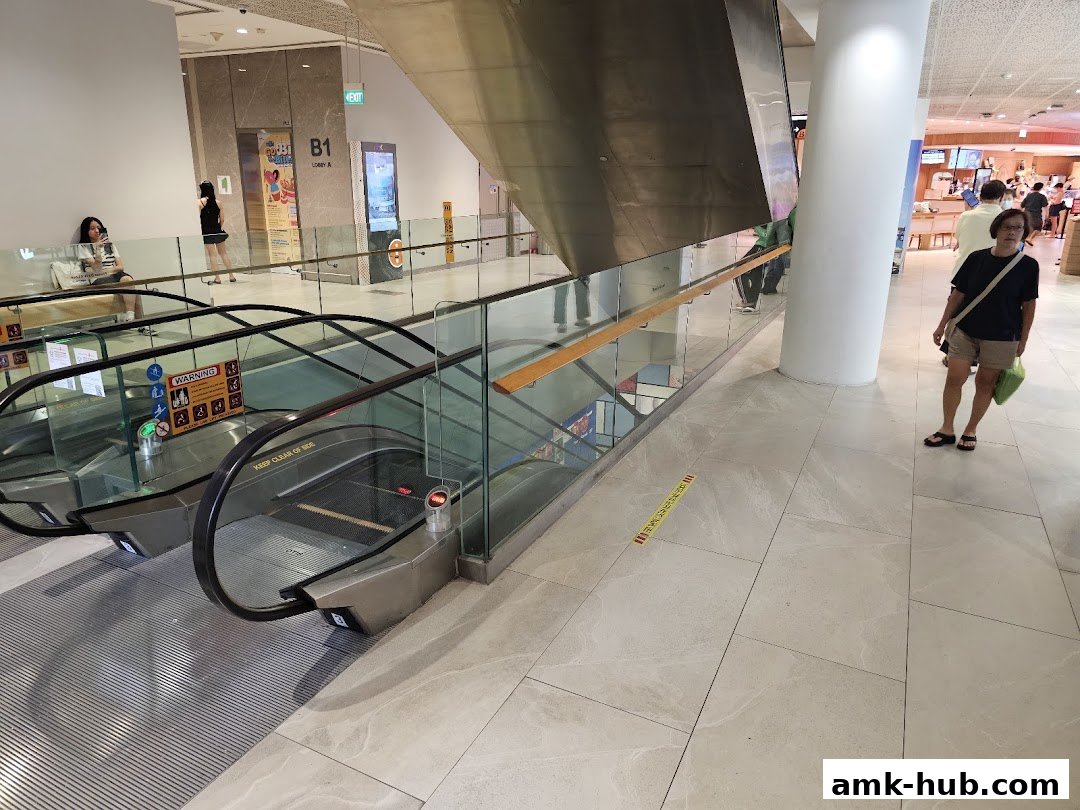 People on escalators and walking in a modern shopping mall with a large pillar.