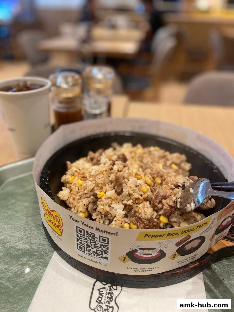 A sizzling Pepper Lunch dish with rice, meat, and corn, served with a drink.
