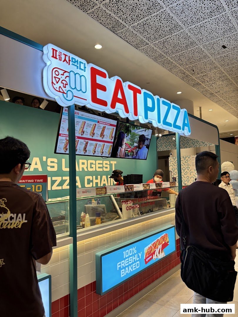 The Eat Pizza shop front with a bright sign and customers waiting.