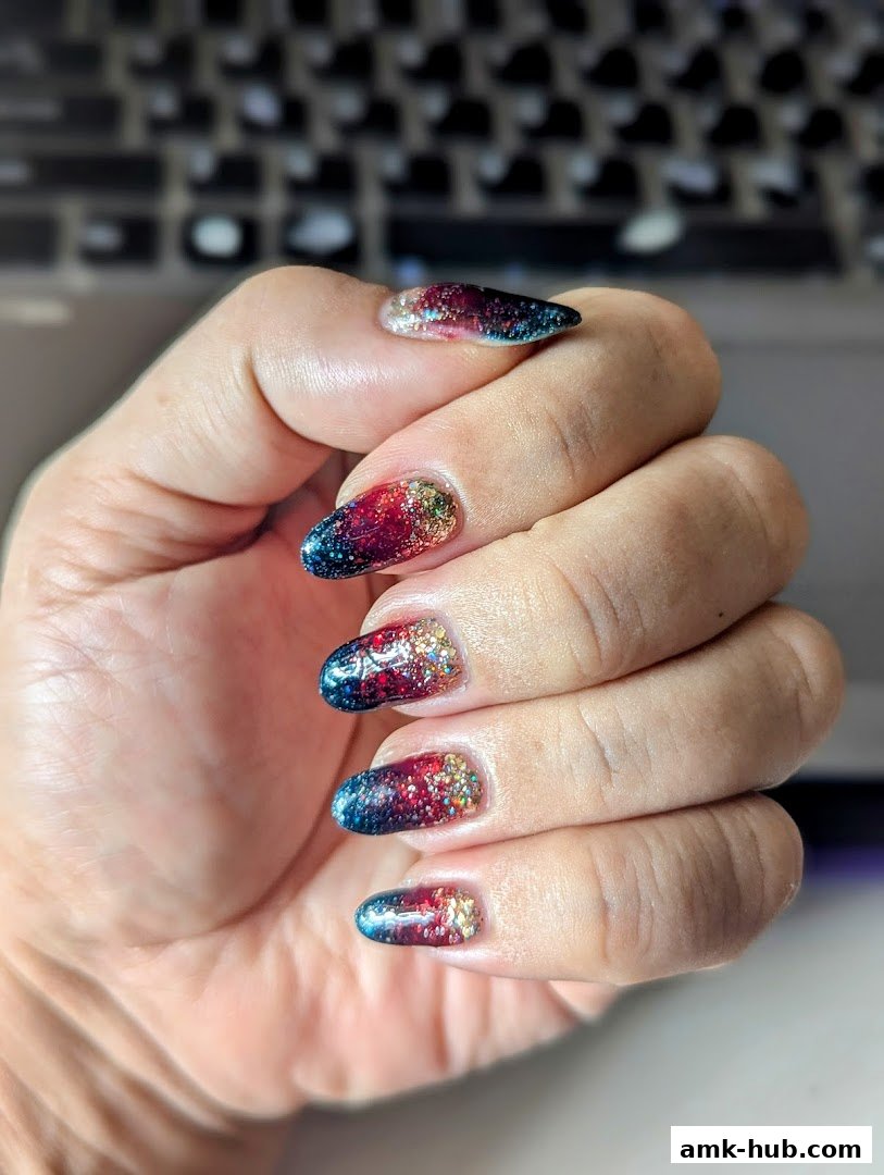 A hand with beautifully decorated nails featuring a galaxy-inspired design with glitter.