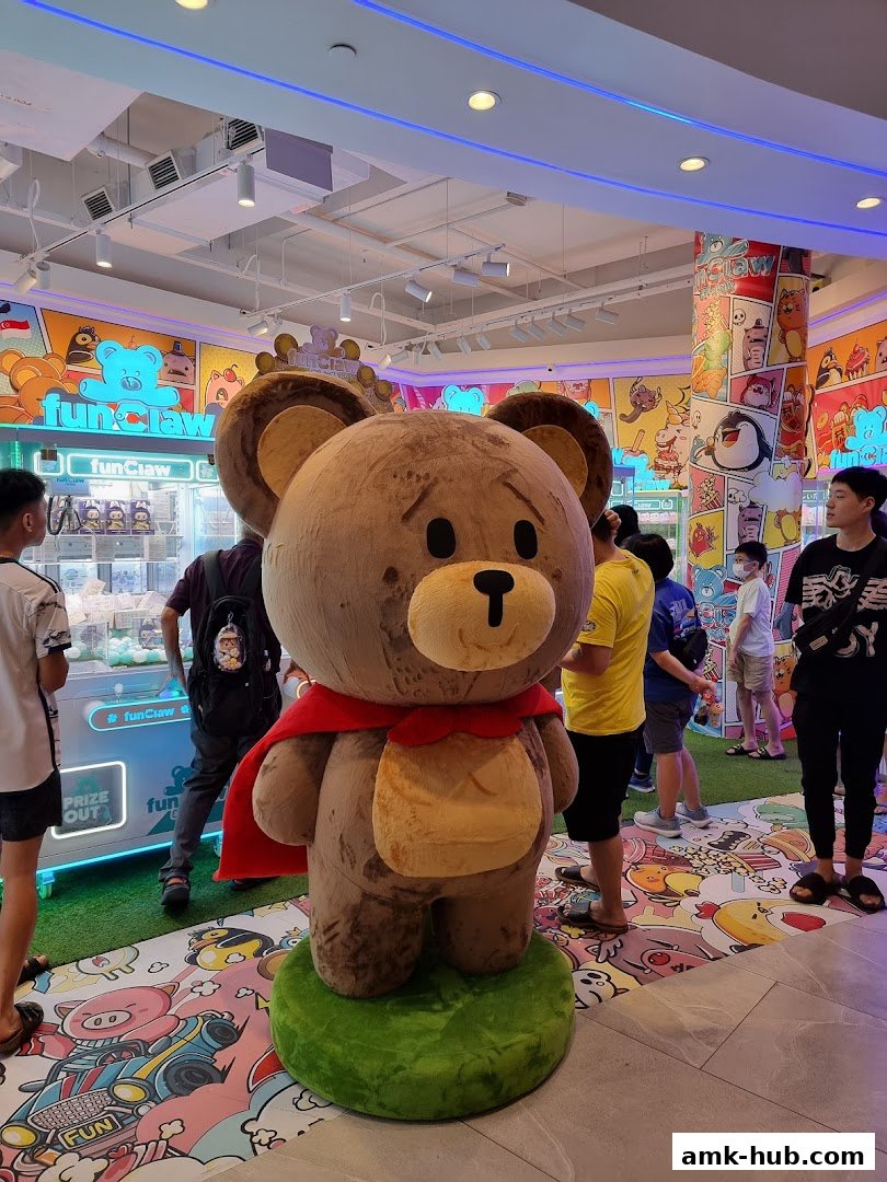 A large teddy bear mascot stands in front of claw machines at the Fun Claw shop.