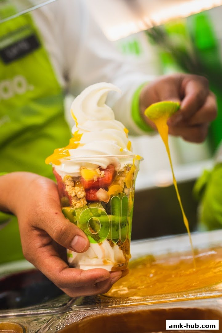 A person is preparing a frozen yogurt cup with fruits and toppings.