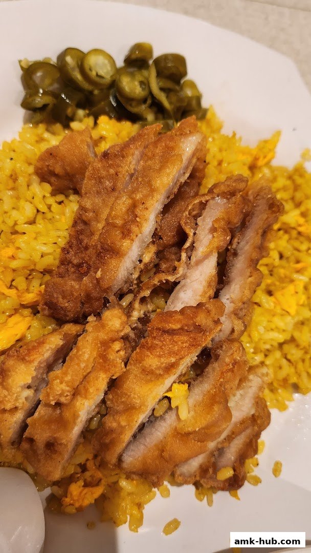 A plate of fried chicken slices served with yellow rice and pickled jalapeños.