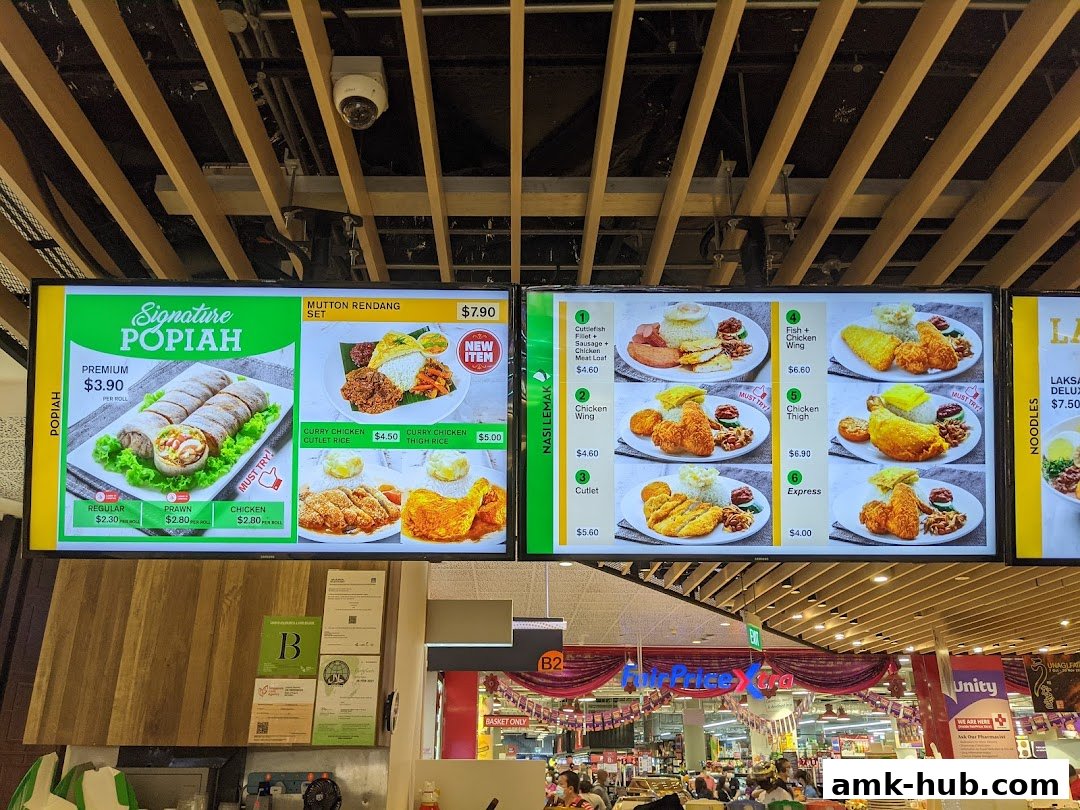 A digital menu board displaying various food items like Popiah, Mutton Rendang, Nasi Lemak, and Noodles.
