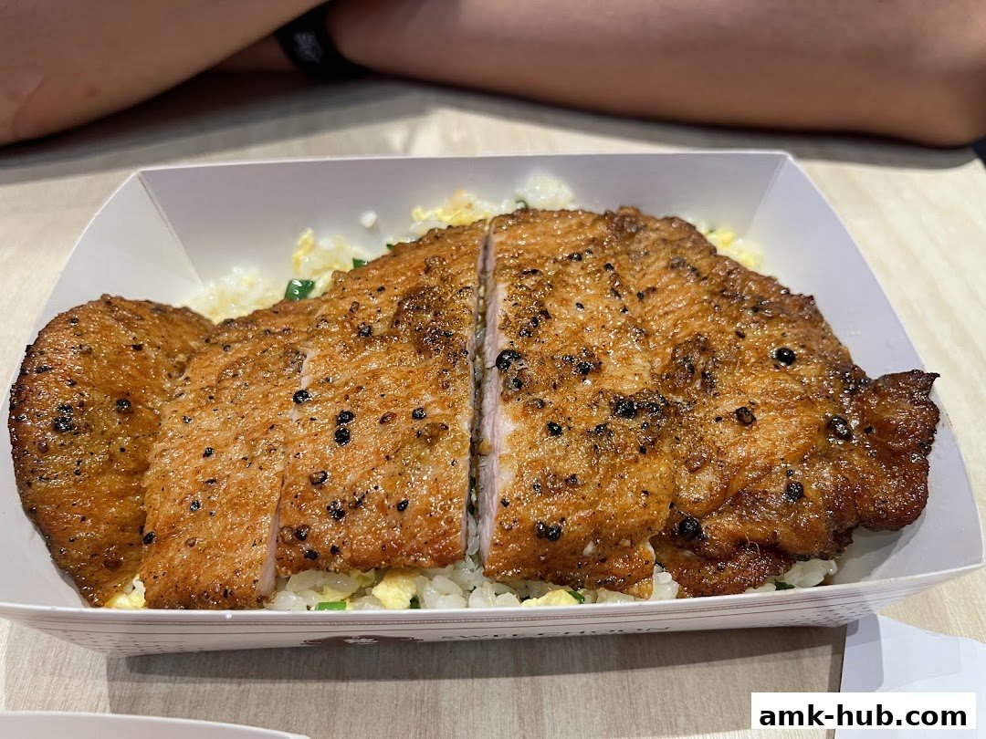 A close-up of a delicious pork chop served over fried rice in a takeout container.