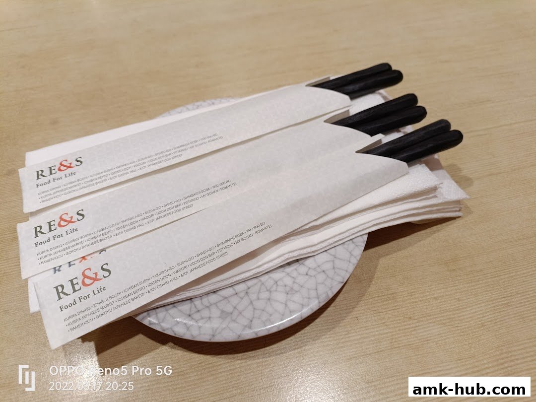 A stack of white chopstick wrappers with black chopsticks on a plate.