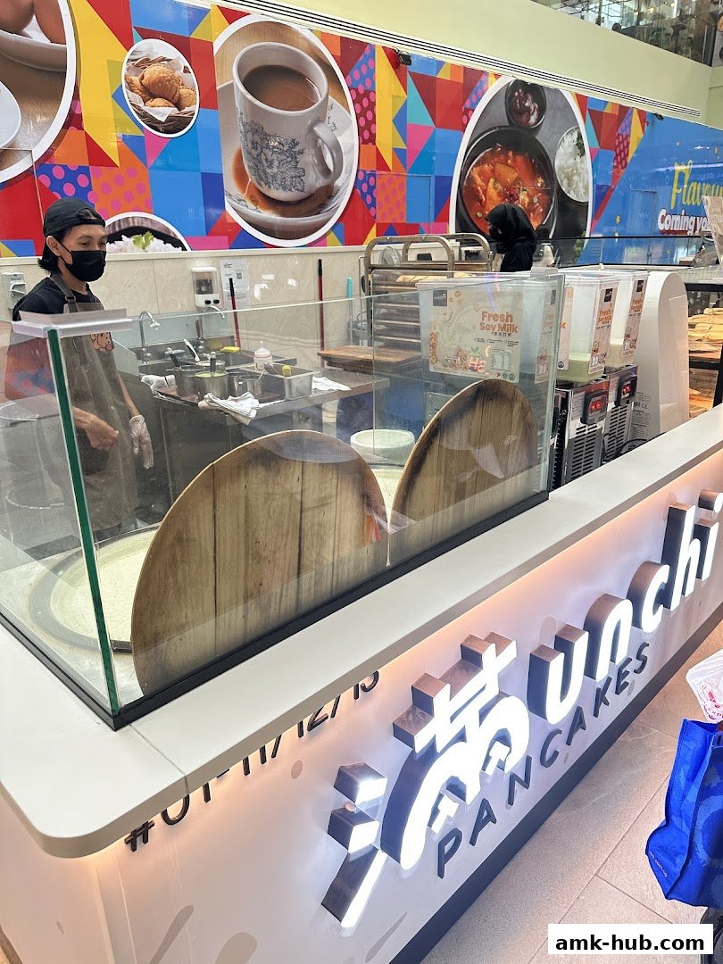 A brightly lit pancake shop counter with staff preparing food and colorful wall art.