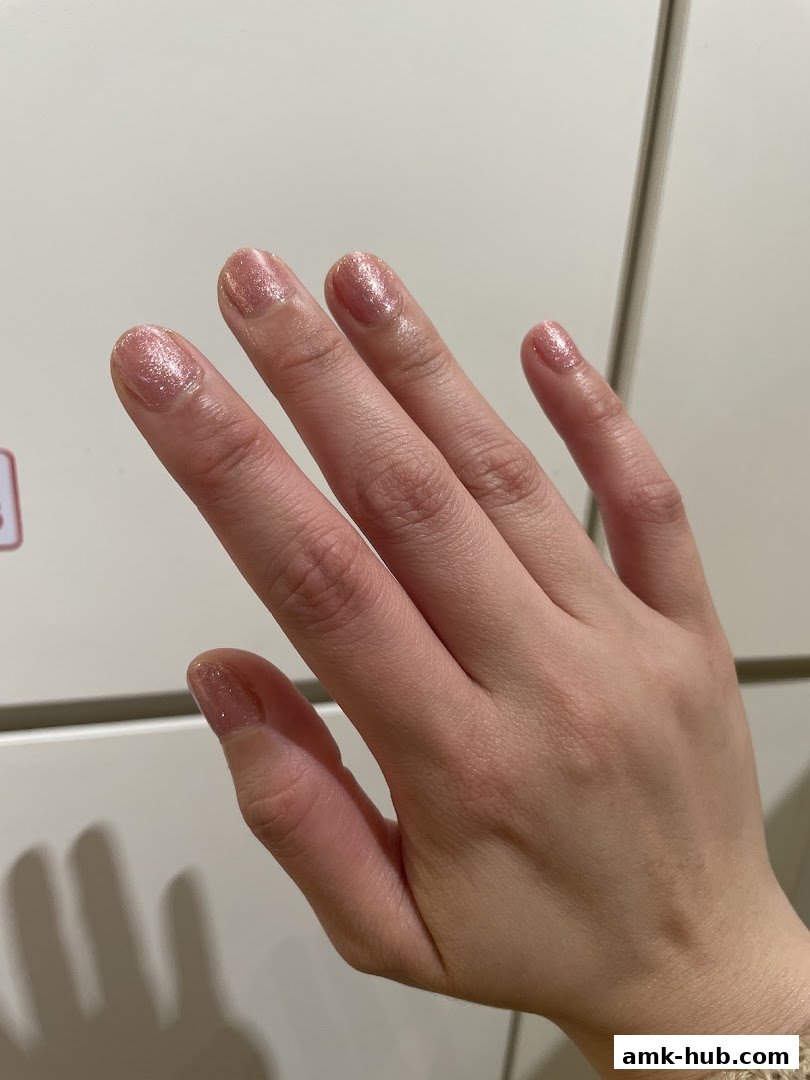 A close-up of a hand with light pink glitter nail polish.