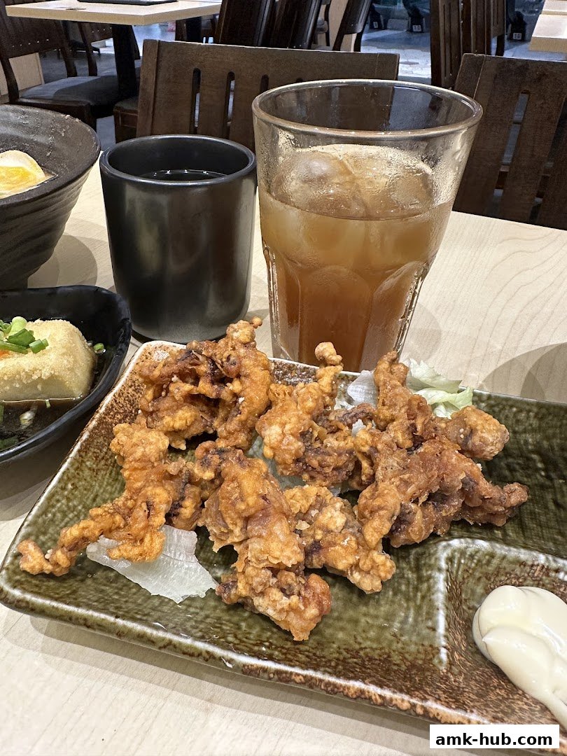 A plate of crispy fried calamari with a side of mayonnaise, served with iced tea and a small dish of tofu.