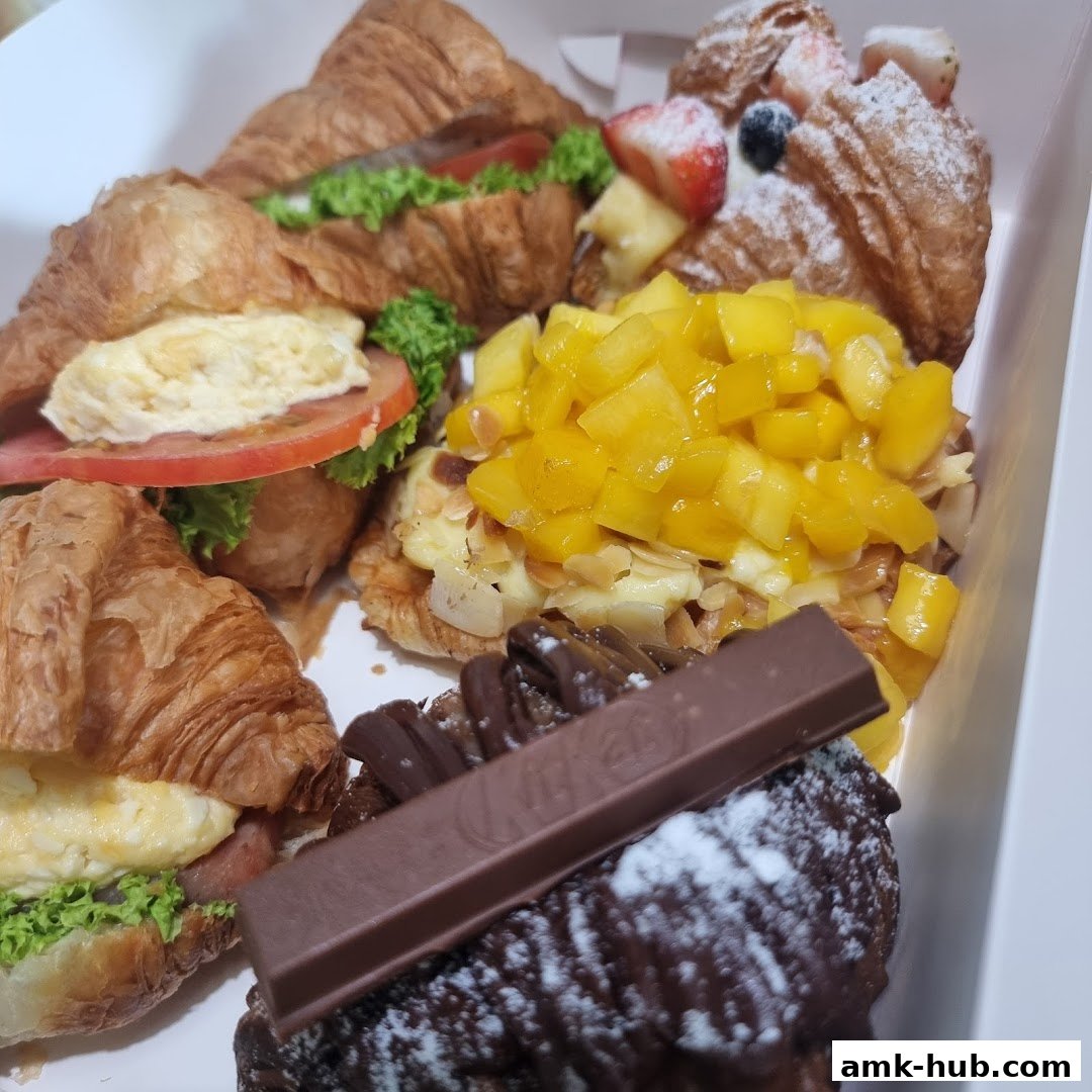 A box filled with various delicious croissants and pastries, including fruit-topped and chocolate-covered options.