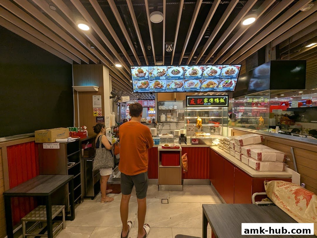 Customers ordering food at a counter with a large menu display and roasted duck.