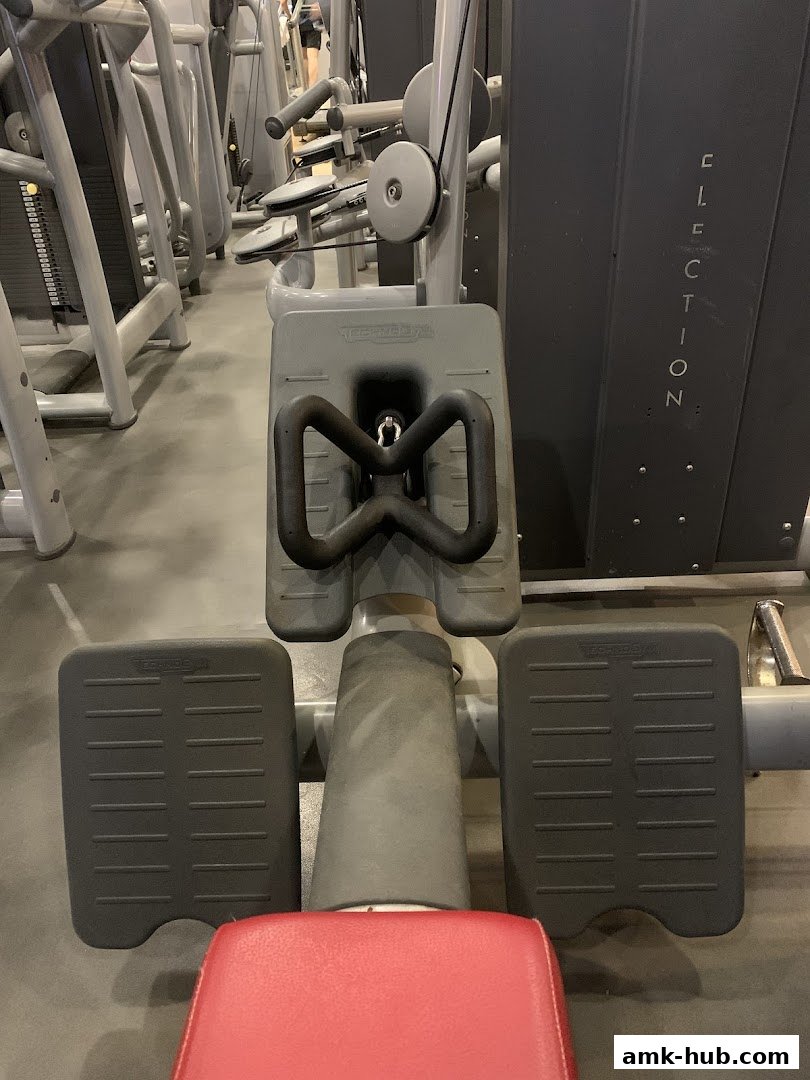 Close-up of a weight machine with a red seat and grey footplates.