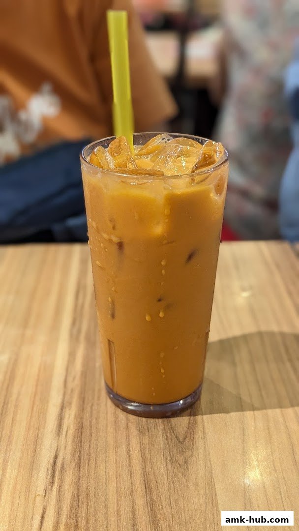 A refreshing glass of iced Thai milk tea with a yellow straw on a wooden table.