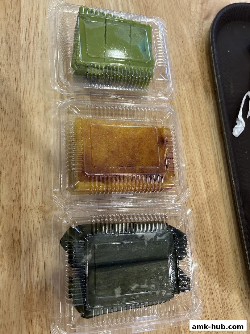 Three individually packaged desserts, one green, one golden, and one dark green, on a wooden surface.