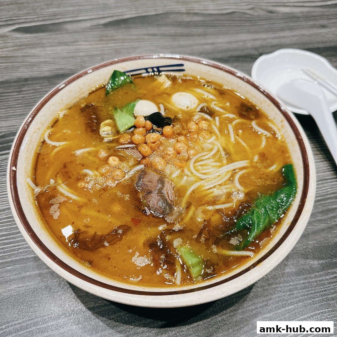 A close-up shot of a steaming bowl of noodle soup with meat and vegetables.
