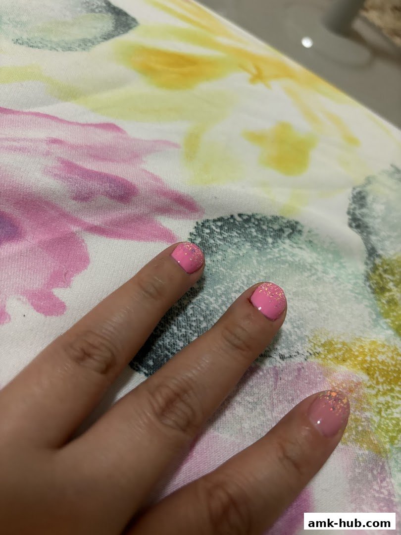 A close-up shot of a hand with freshly painted pink nails with glitter accents.