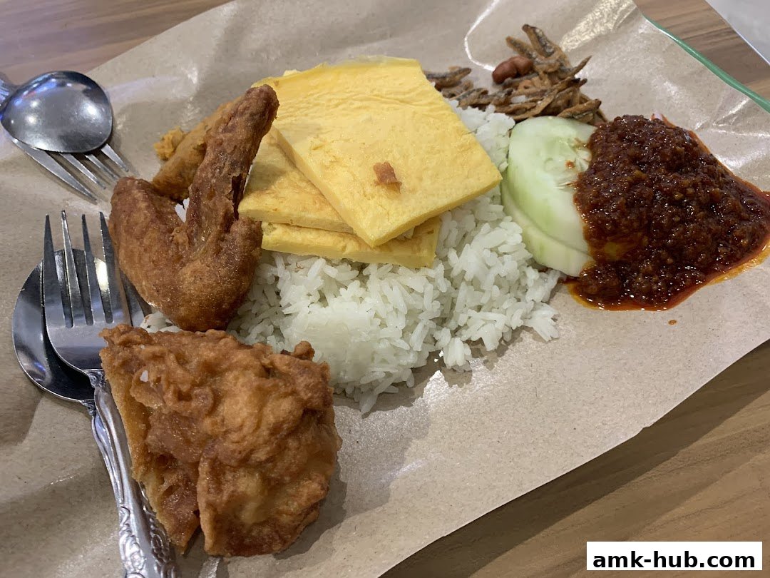A plate of Nasi Lemak with fried chicken, omelette, cucumber, anchovies, and sambal.