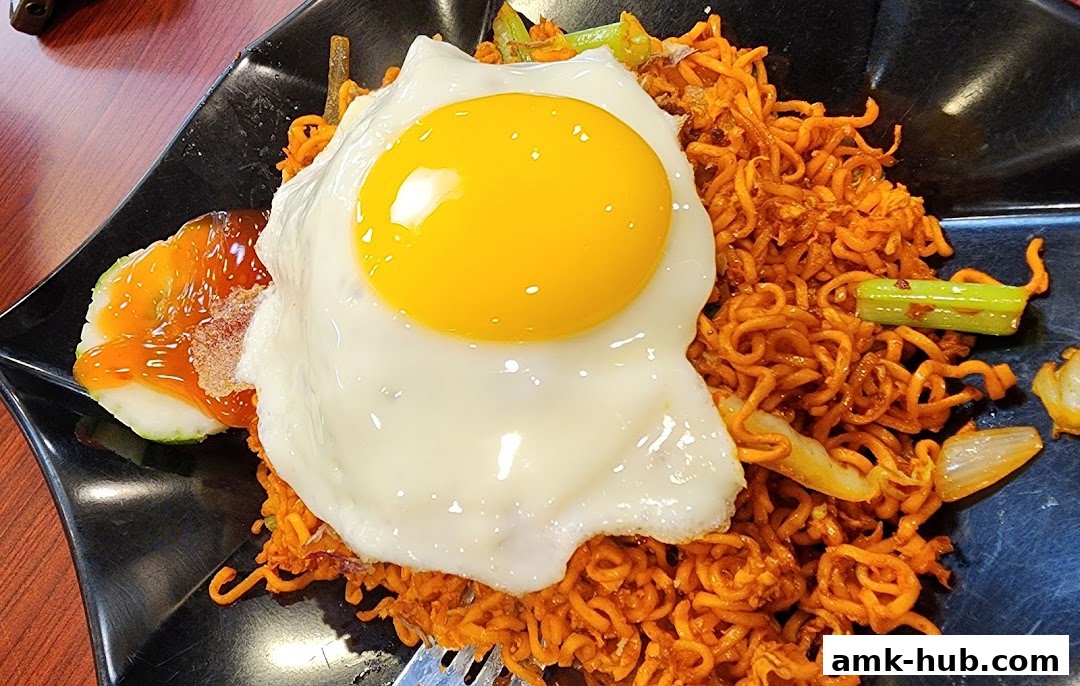 A plate of spicy noodles topped with a sunny-side-up egg and a side of cucumber with sauce.