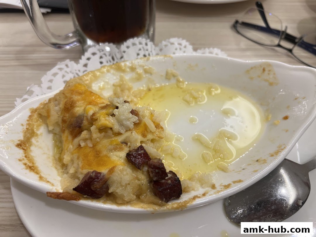 A close-up of a partially eaten cheesy rice dish with bacon and a glass of iced tea.