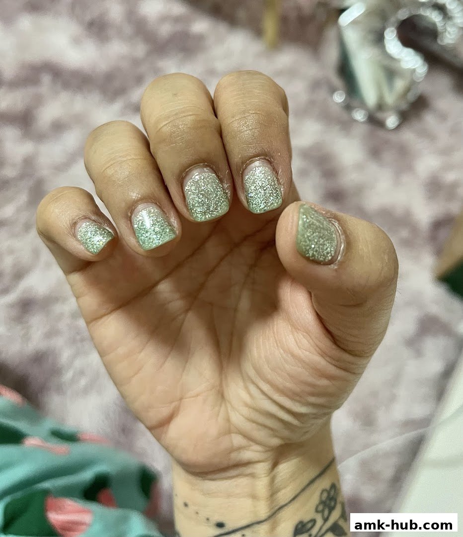 A close-up of a hand with light green glitter gel nails.
