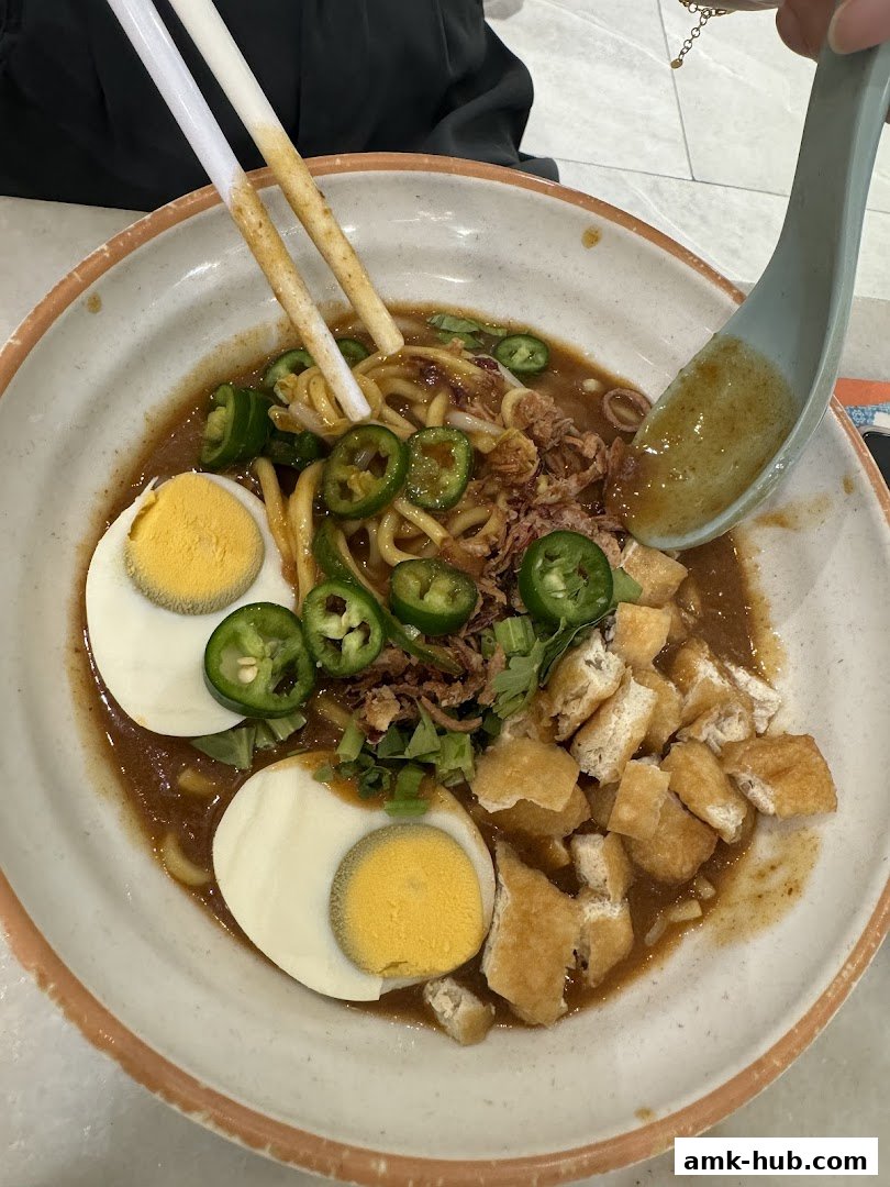 A close-up shot of a delicious bowl of noodles with eggs, tofu, and chili.