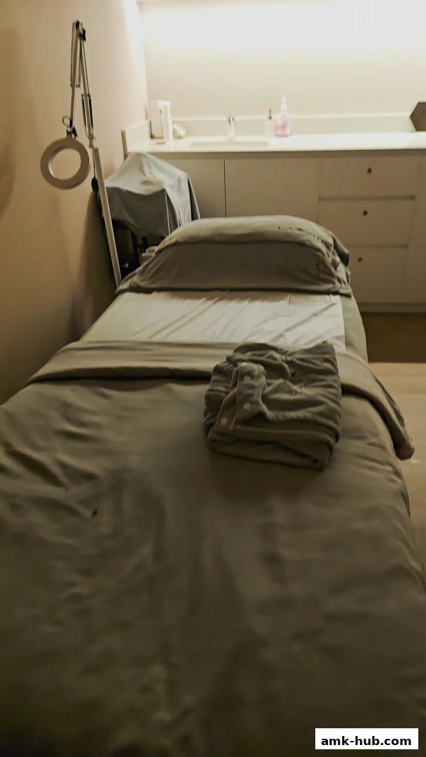 A treatment bed with a folded robe and a magnifying lamp in a clean, well-lit room.