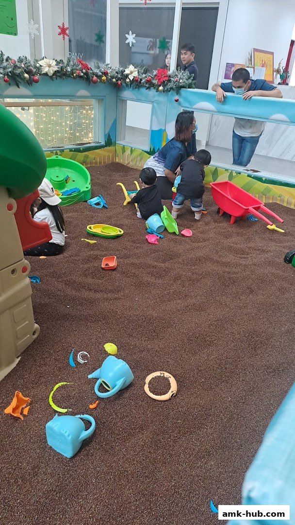 Children playing in a sandpit with toys, supervised by adults.