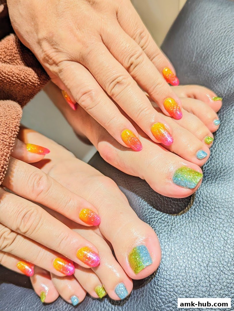 Close-up of hands and feet with vibrant, glittery ombre nail art in sunset colors.