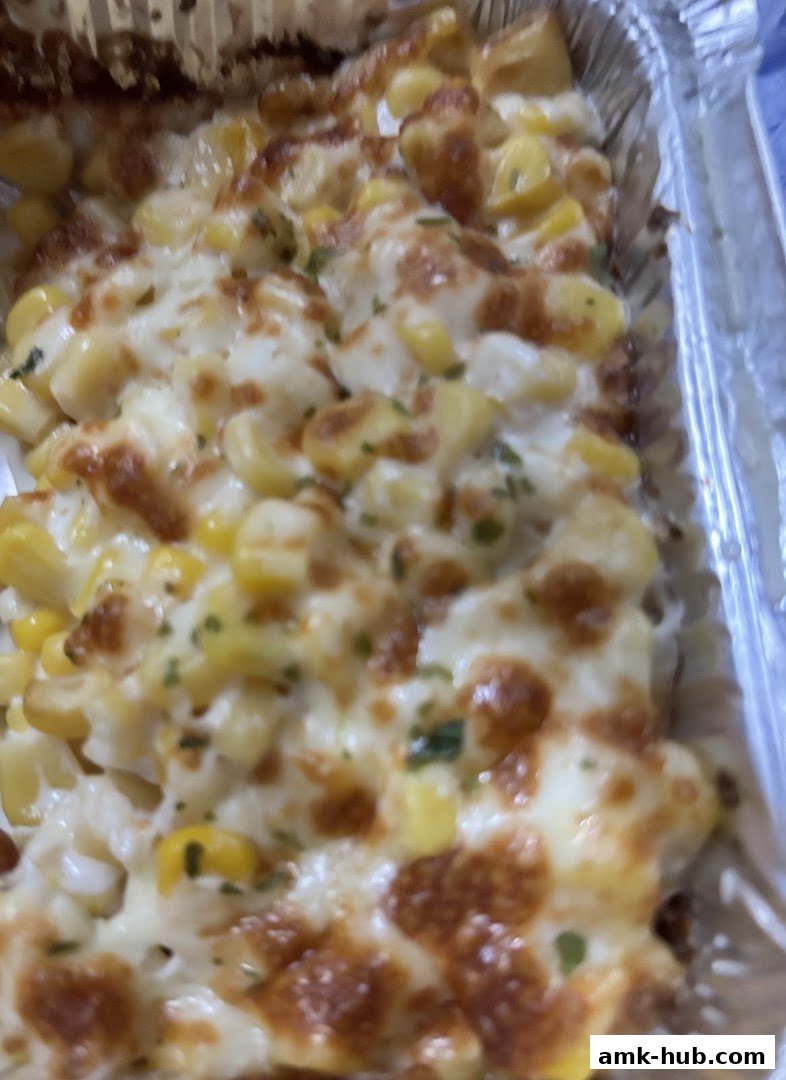 A close-up shot of a cheesy corn dish in a foil container.