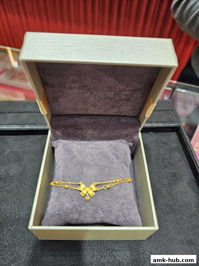 A delicate gold bracelet with a bow and heart charm displayed in an open jewelry box.