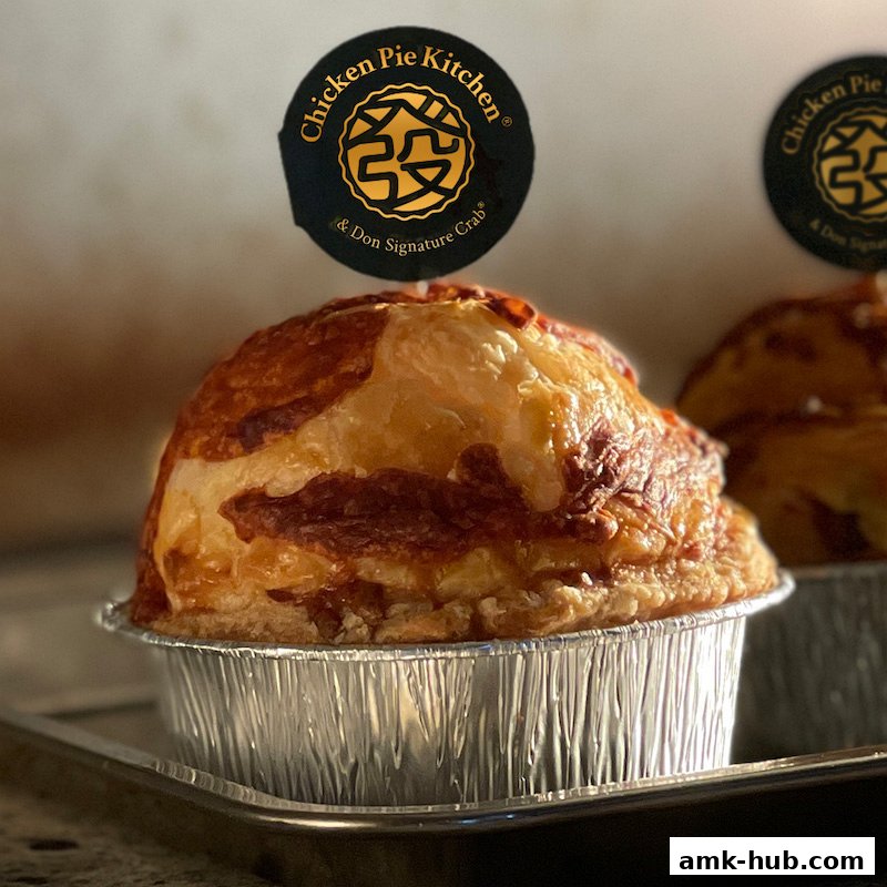 A close-up of a golden-brown chicken pie with a flaky crust, topped with a branded sticker.