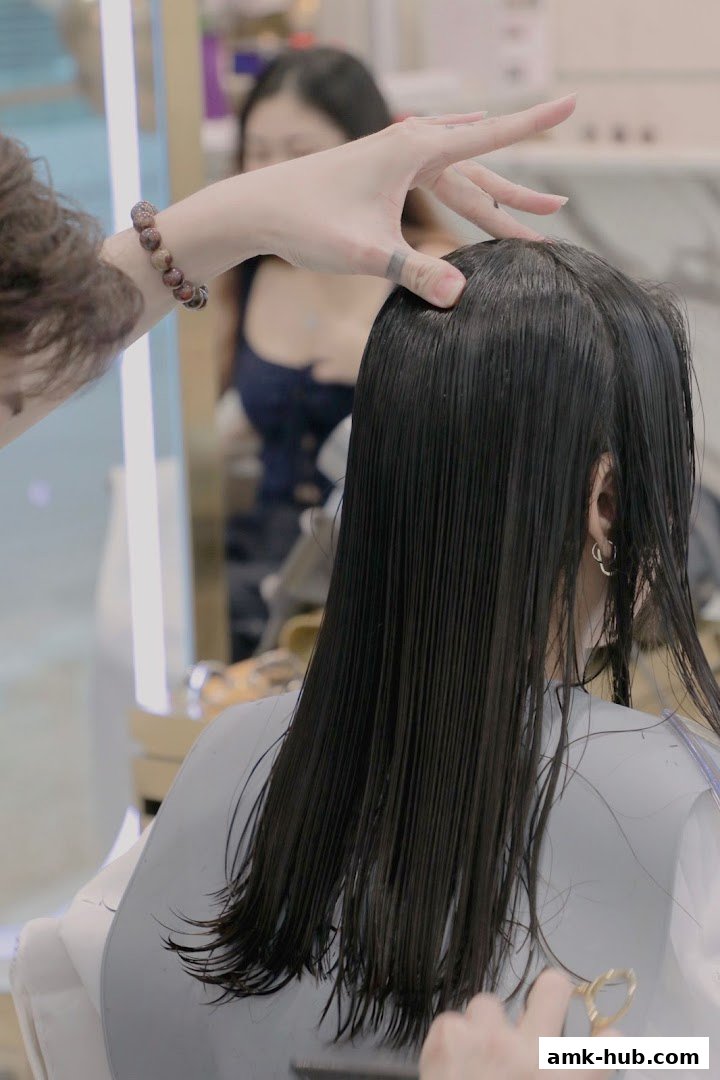 A hairstylist is cutting a client's long, dark, wet hair.