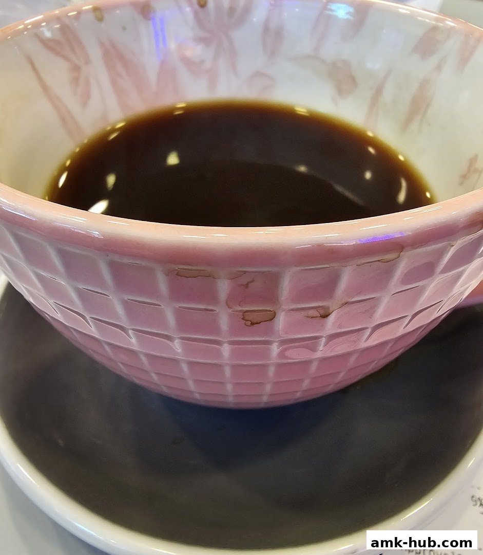 A close-up shot of a pink textured cup filled with dark coffee, resting on a saucer.