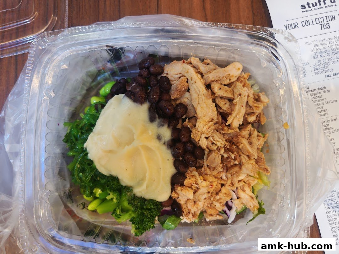 A take-away container filled with a salad featuring chicken, beans, mashed potatoes, and greens.