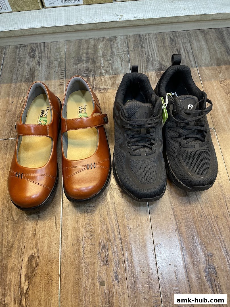 A pair of brown Mary Jane shoes and two pairs of black sneakers are displayed on a wooden floor.