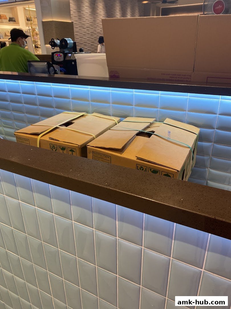 A counter with light blue tiled walls and boxes on top, with staff in the background.