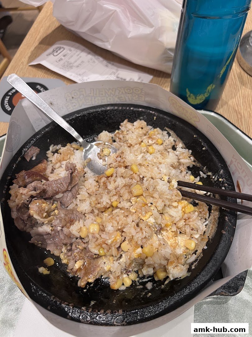 A sizzling hot plate of rice with beef and corn, served with chopsticks and a spoon.