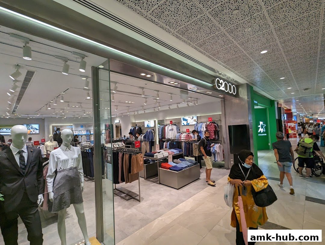 G2000 clothing store interior with mannequins and shoppers browsing merchandise.